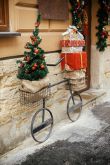 Wall Mural - Stylish minimal bicycle with christmas tree and wrapped gifts in baskets at building exterior. Modern christmas decor in city street. Winter holidays in Europe. Merry Christmas