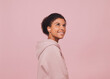 © Picture Store - Smiling young black woman listening music. Portrait of happy girl in pink hoodie with wireless headphones against pink backdrop