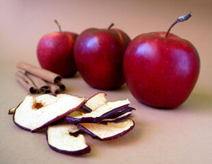 Wall Mural - a few chips from dried apples lie on a brown background next to cinnamon sticks against the background of three juicy red apples front view.  food