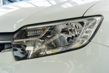 Close-up Of Right Front Headlight Of White Renault Logan Stepway Car In Showroom Of A Renault Dealership. Renault Showroom In Mega Adygea