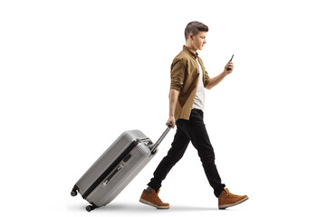 Wall Mural - Full length profile shot of a guy with a smartphone pulling a suitcase