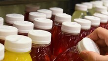 Woman Hand Selects Fresh Squeezed Juice In Plastic Bottle Of Different Colors, Filled With Vitamins From Different Fruits And Vegetables At Supermarket. Closeup.
