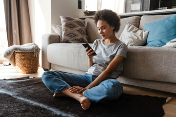 Wall Mural - Young beautiful smiling curly african woman holding and using phone