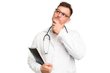 Young doctor caucasian man holding a book isolated looking sideways with doubtful and skeptical expression.