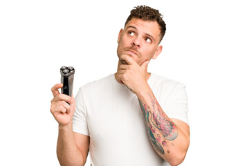 Young caucasian man holding a razor isolated looking sideways with doubtful and skeptical expression.