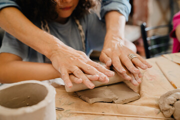 Wall Mural - Close up of hands rolling clay with a wooden rolling pin at workshop