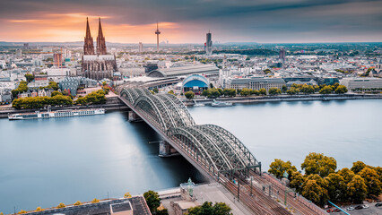 Cologne Aerial view with trains move on a bridge over the Rhine River on which cargo barges and passenger ships ply. Majestic Cologne Cathedral in the background