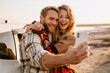© Drobot Dean - Happy white couple taking selfie photo by car while walking at seashore
