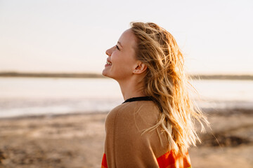 Happy young white woman smiling while walking by seashore on sunny day