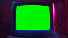 Close Up Footage Of A Dated TV Set With Green Screen Mock Up Chroma Key Template Display. Nostalgic Retro Nineties Technology Concept. Vintage Television Display In Neon Lit Living Room.
