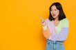 Upset asian girl pointing at copy space isolated over yellow background
