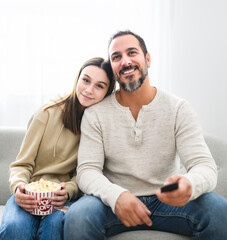 father and teen girl watching television while eating pop corn at home