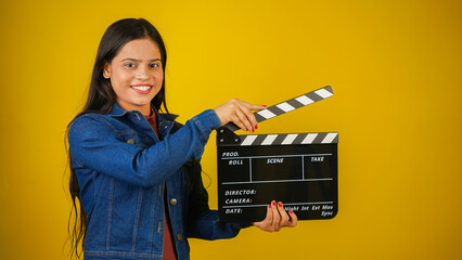 Beautiful young Asian Indian woman standing holding clapperboard, clapper board used in film making, isolated on color background studio portrait