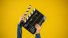 Hand Is Holding Clapper Board Or Clapperboard Or Movie Slate, Used In Film Production And Cinema ,movies Industry Isolated Over Yellow Background.