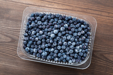 Canvas Print - Transparent plastic bowl full of big ripe blueberries on dark wooden background. Healthy food for winter, vitamins and juicy sweet snack concept