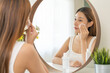 Happy beauty, attractive asian young woman, girl looking reflect in mirror, hand holding cotton pad, applying facial wipe on her face remover makeup, essence or lotion for treatment, skin care routine