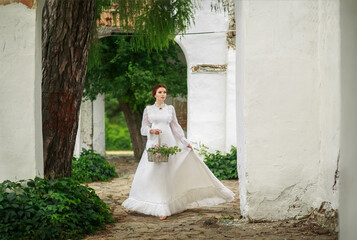 Wall Mural - Beautiful girl in a vintage long white dress, and a hairstyle in the English style in a summer park, against the background of columns, warm summer