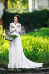 Wall Mural - Beautiful girl in a vintage long white dress, and a hairstyle in the English style in a summer park, against the background of columns, warm summer