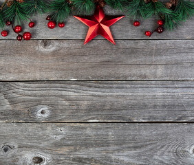 Wall Mural - Merry Christmas or happy New Year background with fir tip branches and red star decoration on rustic wood