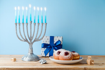 Wall Mural - Jewish holiday Hanukkah concept with menorah, traditional donuts and gift box on wooden table.