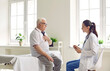 © Studio Romantic - Agitated elderly man with glasses holds his hand on his chest, talking to a doctor in white coat, sitting on medical couch. Beautiful young female doctor supports unhealthy elderly man on consultation