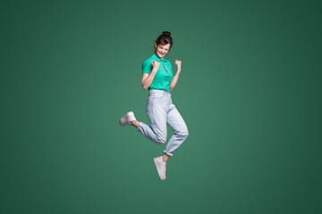 Full length portrait of attractive lovely pretty lucky girl celebrating success while jumping isolated over green background. Happiness, win, success.