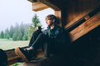 © Soloviova Liudmyla - Young lonely teenager boy drinking hot tea from thermo flask while he sitting on the wooden forest house terrace and enjoying the morning spruce foggy forest. Traveling and tourism at fall time.