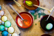 Dyed Easter Eggs Rest In A Cardboard Egg Container, While The Remnants Of Organic Natural Food Coloring Dyes Rest In Bows Of Hot Water, Vinegar And Spoons.
