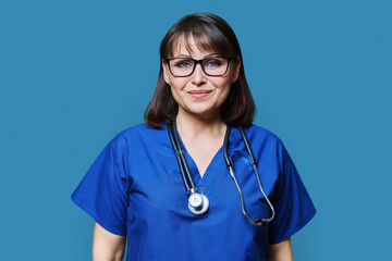 Wall Mural - Middle aged female nurse in blue uniform with stethoscope smiling looking at camera