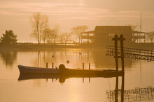 A Dock And Motor Boat Are Silhoutted In The Golden Light Of The Rising Sun.