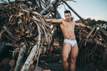 Muscular Man In Briefs Leaning Against Dry House-shaped Trees