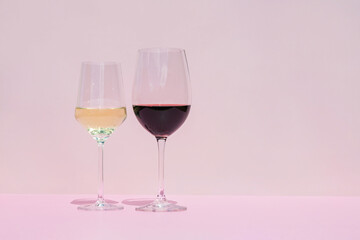 Wall Mural - A glass of red and white wine on a pink background in the bright rays of the sun.