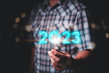 Fototapete - Male hand holding light bulb with numbers 2023 showing new ideas for next year.