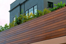 Wood Slatted Wall Or Barrier With Gray House Facad And Windows With Black Accent Paint On Cloudy Background