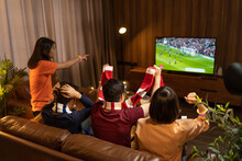 Group Of Asian People Friends Sit On Sofa Watching And Cheering Football Or Soccer Games Competition On TV Together At Home.Happy Man And Woman Sport Fans Celebrating Sport Team Victory Sports Match