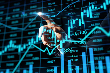 Close up of businessman hand pointing at glowing business chart hologram and index on blurry background. Finance, trade and invest concept. Double exposure.