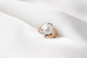 Pearl ring with golden fittings on shiny white silk background. Beautiful accessories for women. Elegant jewelery gift or present for wedding or saint valentine's day.