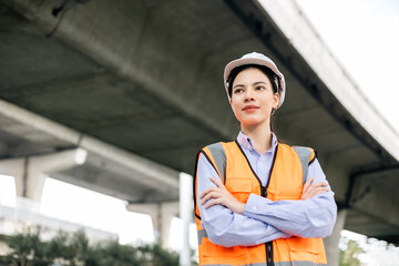 Wall Mural - Asian engineer worker woman or architect looking construction with white safety helmet in construction site. Standing at highway concrete road site. Progress planning of highway bridge.