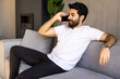 © dianagrytsku - Cheerful arab man talking on smartphone resting on sofa at home interior