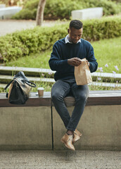 Poster - Business man eating food for lunch on his break outdoors at a park opening a brown paper bag. Hungry, happy black male time to eat and drink outside in the city. Enjoying a takeaway or takeout meal