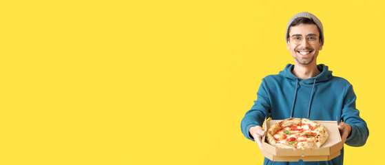 Wall Mural - Happy young man with tasty pizza on yellow background with space for text