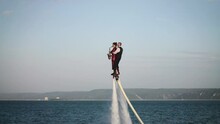 Show Over The Water On A Flyboard. A Woman In A Red Dress Plays The Saxophone, A Man Flies With Her Together.