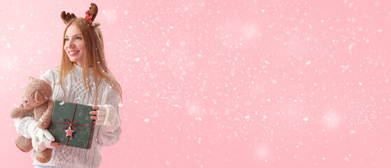 Poster - Young woman with Christmas present, toy and falling snow on pink background with space for text