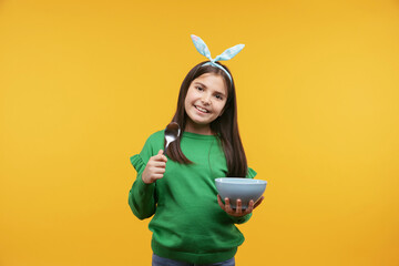 Studio portrait of smiling kid girl holding a bowl of cereal and spoon, breakfast, healthy eating and nutrition for children concept. Isolated on yellow background.