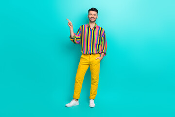 Sticker - Full length photo of young satisfied smiling guy wear striped colorful shirt finger direct empty space useful tips isolated on cyan color background