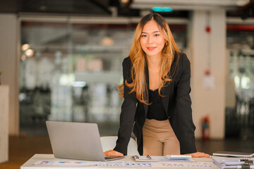 Asian businesswoman with laptop and financial graph in analyzing in office Beautiful girl with tablet computer and checkbook paying bills happily starting business finance calculation concept