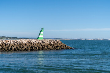 Lighthouse on a rock pier painted in green and white. Blue ocean and sky