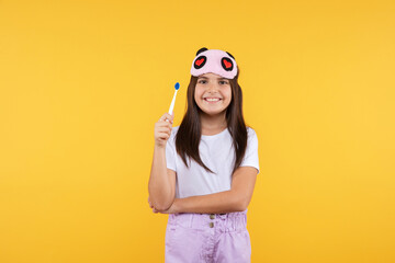  Studio shot of smiling little girl in white t-shirt and eye mask holding  toothbrush looking to the camera. Morning routin and kids hygiene concept.