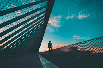 silhouette of the cyclist on the bridge, person riding trough the bridge