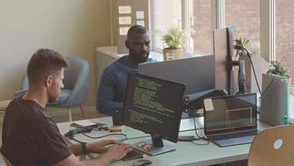 Two multiethnic software engineers program coding on desktop computers during work in modern office
